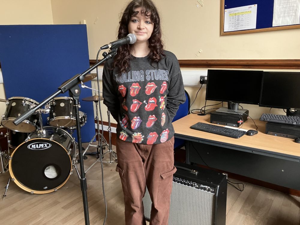 A student at a microphone with musical instruments in the background